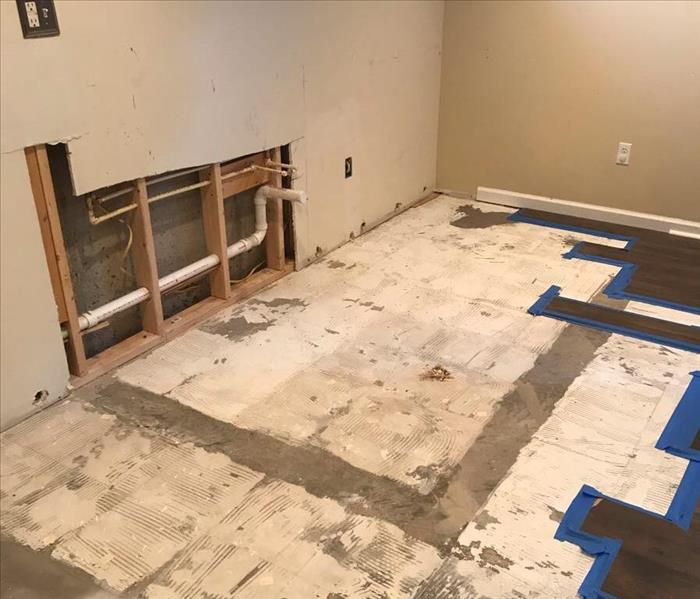 Exposing plumbing in the wall, surrounded by open tile floors due to water damage.