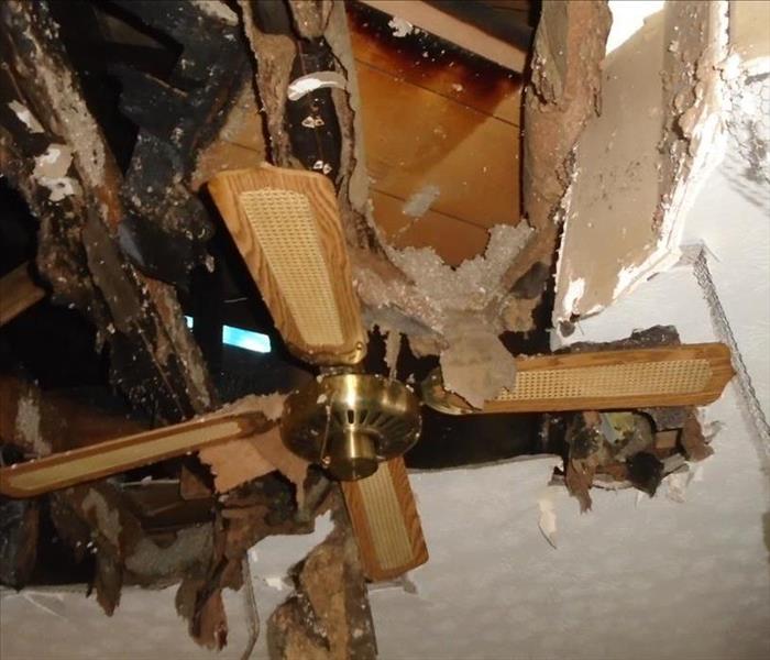 A ceiling with fire damage, the fan barely hanging up.