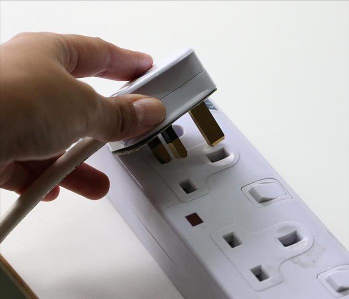 A hand is plugging a cord into an electrical outlet on a table.