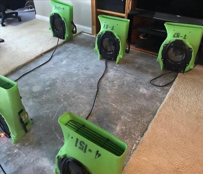 Five air movers sit over a carpet-less area in a living room.