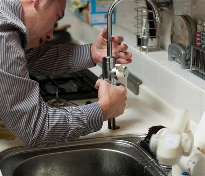 A contractor repairs the faucet of a kitchen sink.