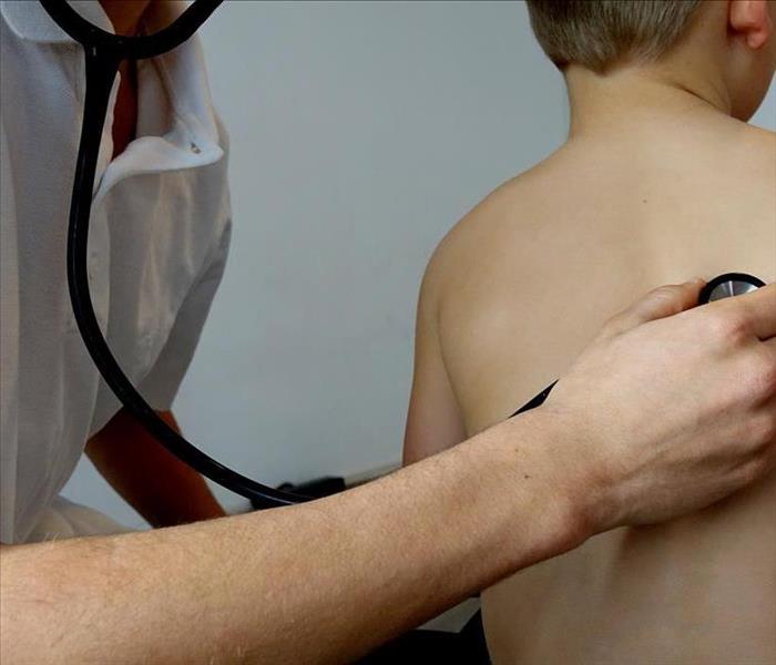 A doctor presses the stethoscope against the back of a child.