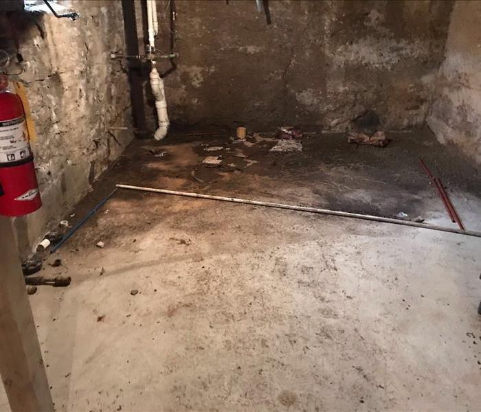 Basement floor with burn marks from fire damage, beside a fire extinguisher mounted to a post.